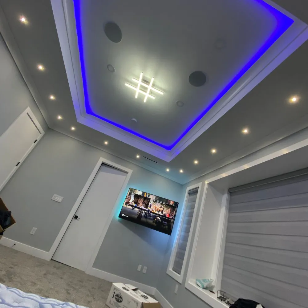 Modern room with recessed ceiling lighting and a tray ceiling featuring blue RGB LED accent lighting, complemented by wall sconces and spotlights, showcasing a clean and contemporary RGB mood lighting installation.
