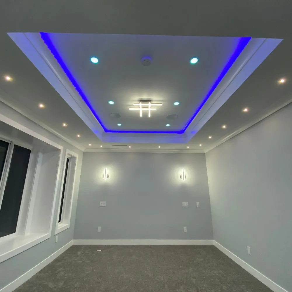 Modern room with recessed ceiling lighting and a tray ceiling featuring blue RGB LED accent lighting, complemented by wall sconces and spotlights, showcasing a clean and contemporary RGB mood lighting installation.