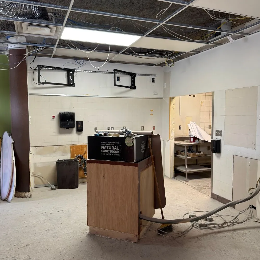 Interior commercial space under renovation in North Vancouver, featuring exposed ceiling wiring, open wall cavities, temporary equipment, and loose electrical conduits on the floor, documenting the site before a commercial electrical installation upgrade.
