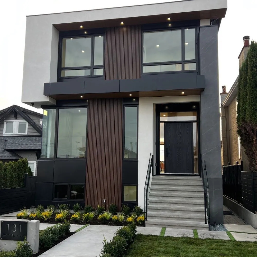Modern two story Burnaby home with contemporary exterior lighting, including recessed soffit lights that highlight the facade, vertical wood paneling, large windows, and a wide front entry staircase with clean landscaping.